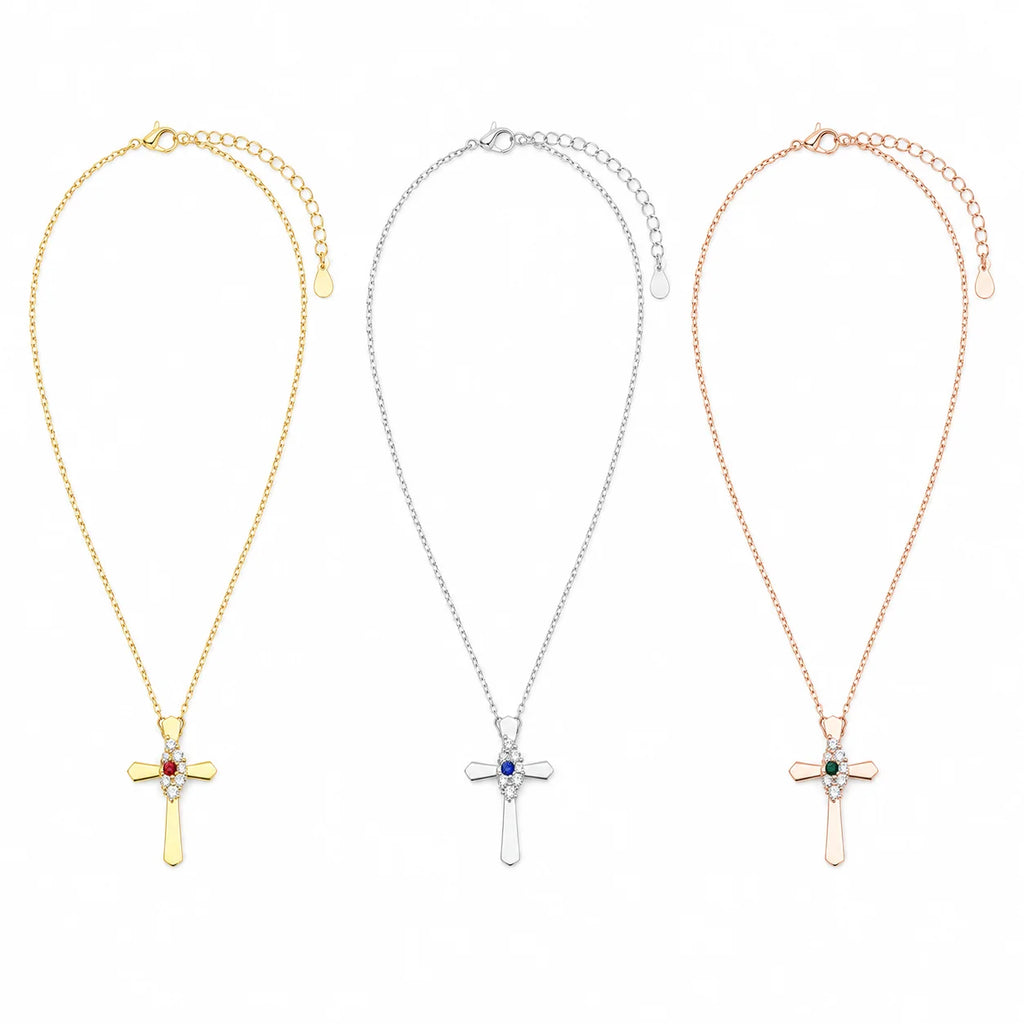 Three cross pendant necklaces shown side by side on a white background, each with a delicate chain and adjustable clasp. The left necklace is gold with a small red gemstone, the center is silver with a blue gemstone, and the right is rose gold with a green gemstone.