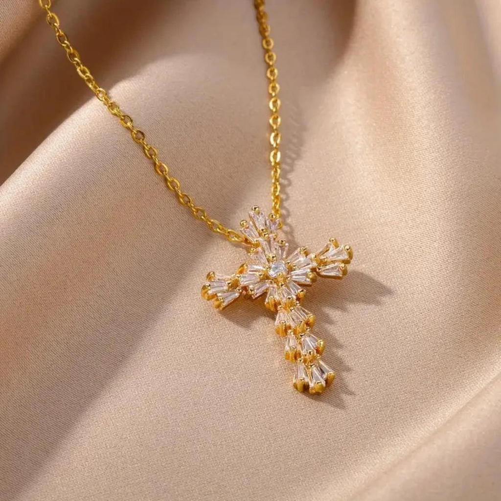Gold cross necklace with clear gemstones on a beige fabric background