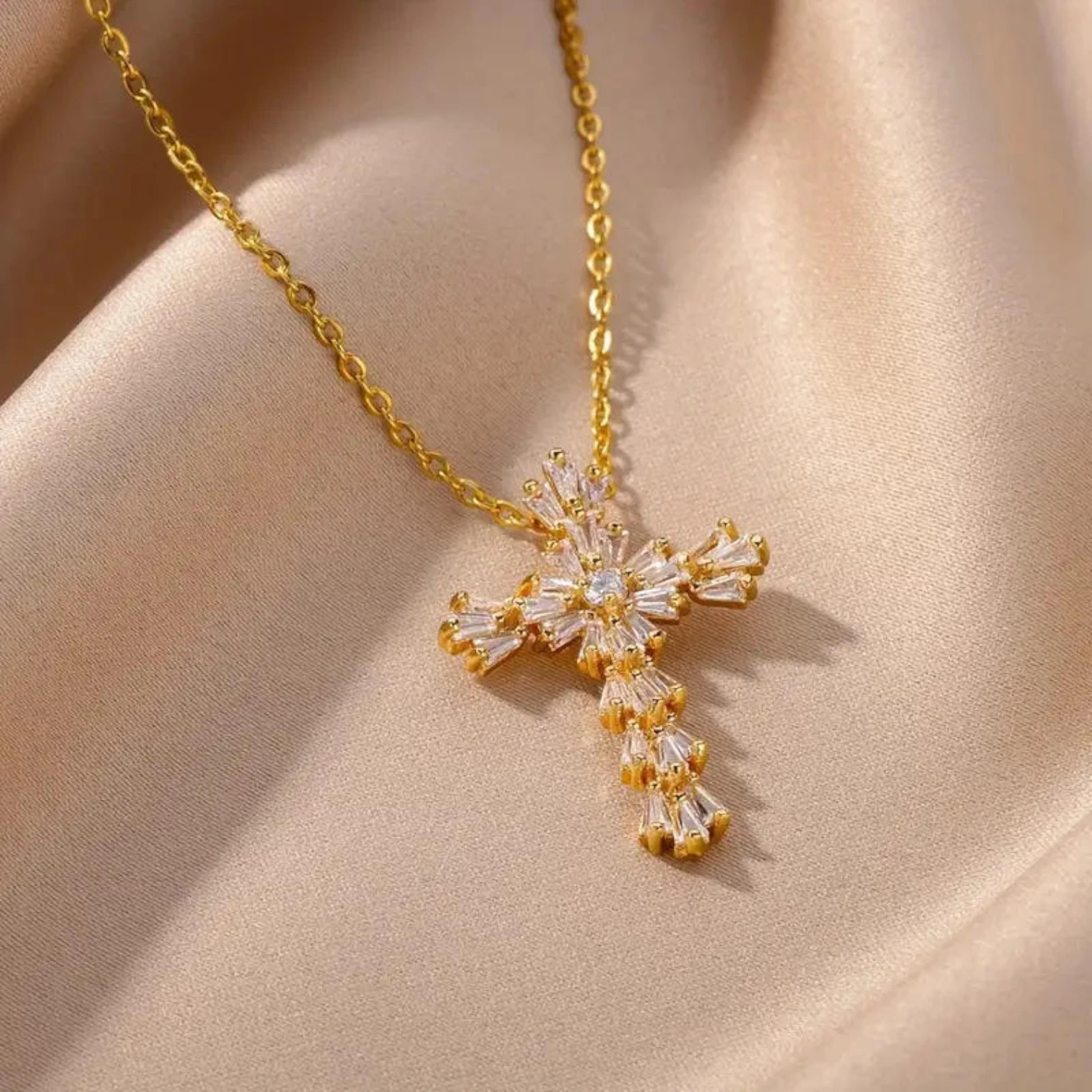 Gold cross necklace with clear gemstones on a beige fabric background