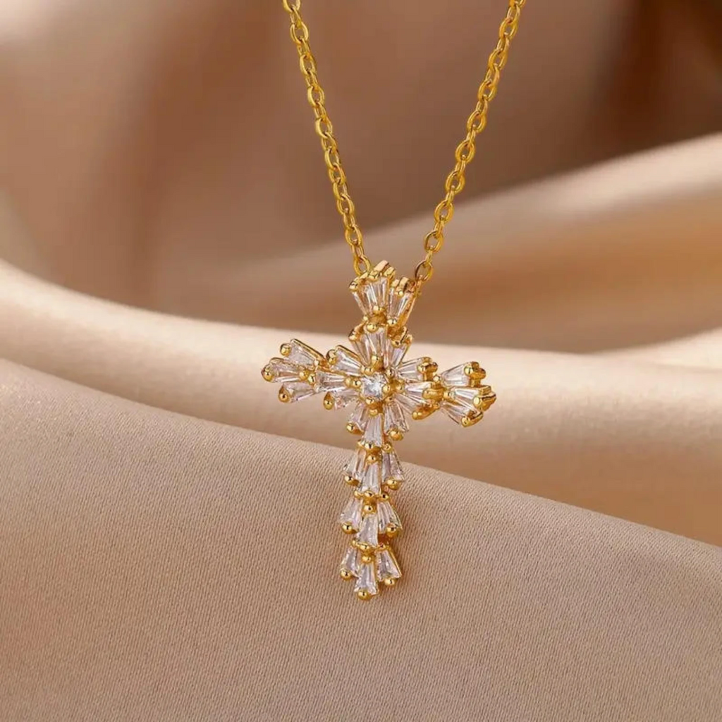 Gold cross necklace with clear stones on a beige fabric background