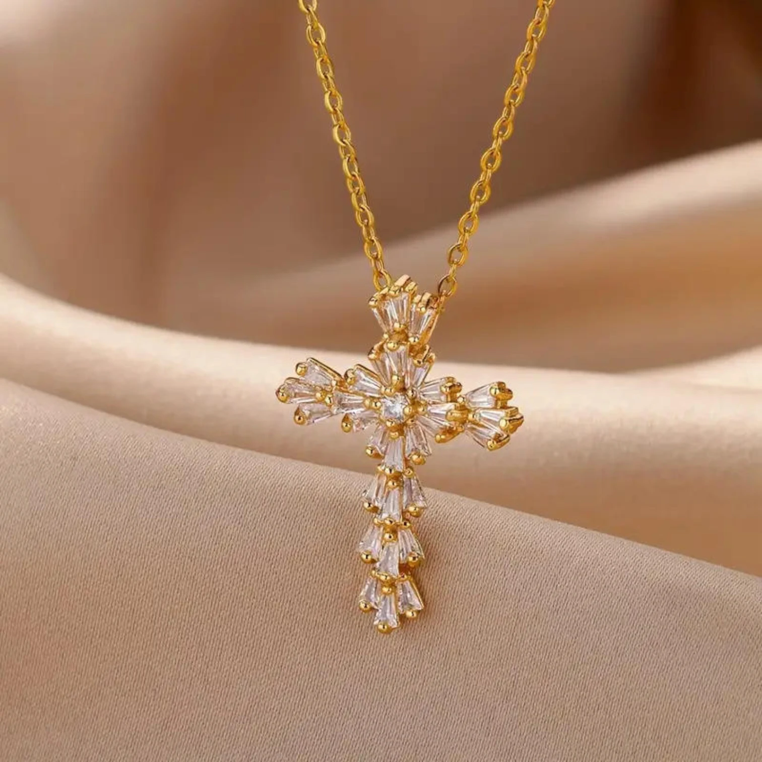 Gold cross necklace with clear stones on a beige fabric background