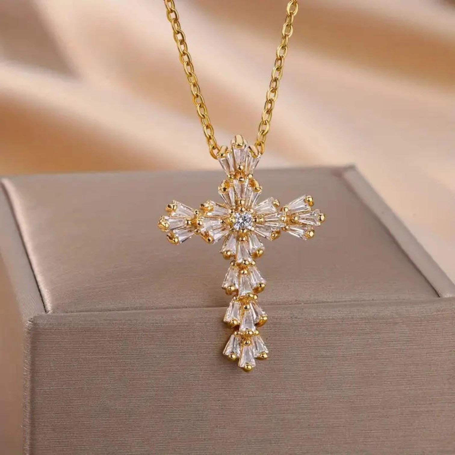 Gold and crystal cross necklace on a beige background