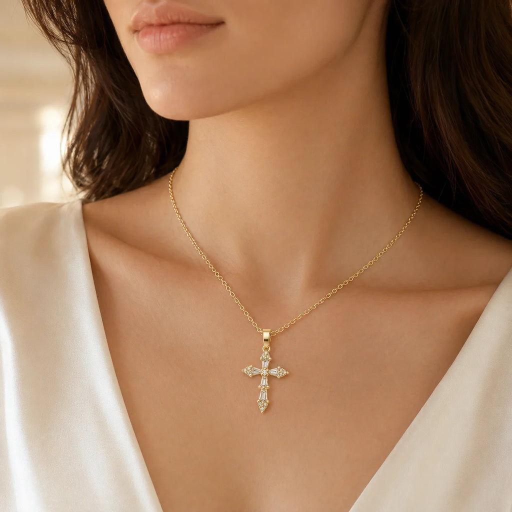 A close-up of a woman wearing a delicate gold cross pendant necklace adorned with small clear stones, styled with a white satin top.