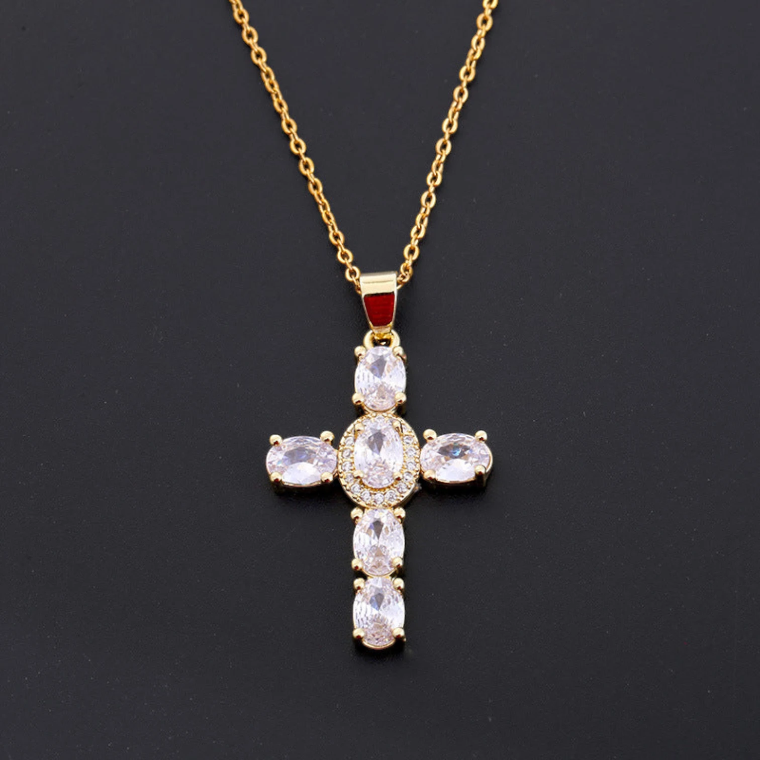 Gold cross pendant necklace with clear stones on a black background