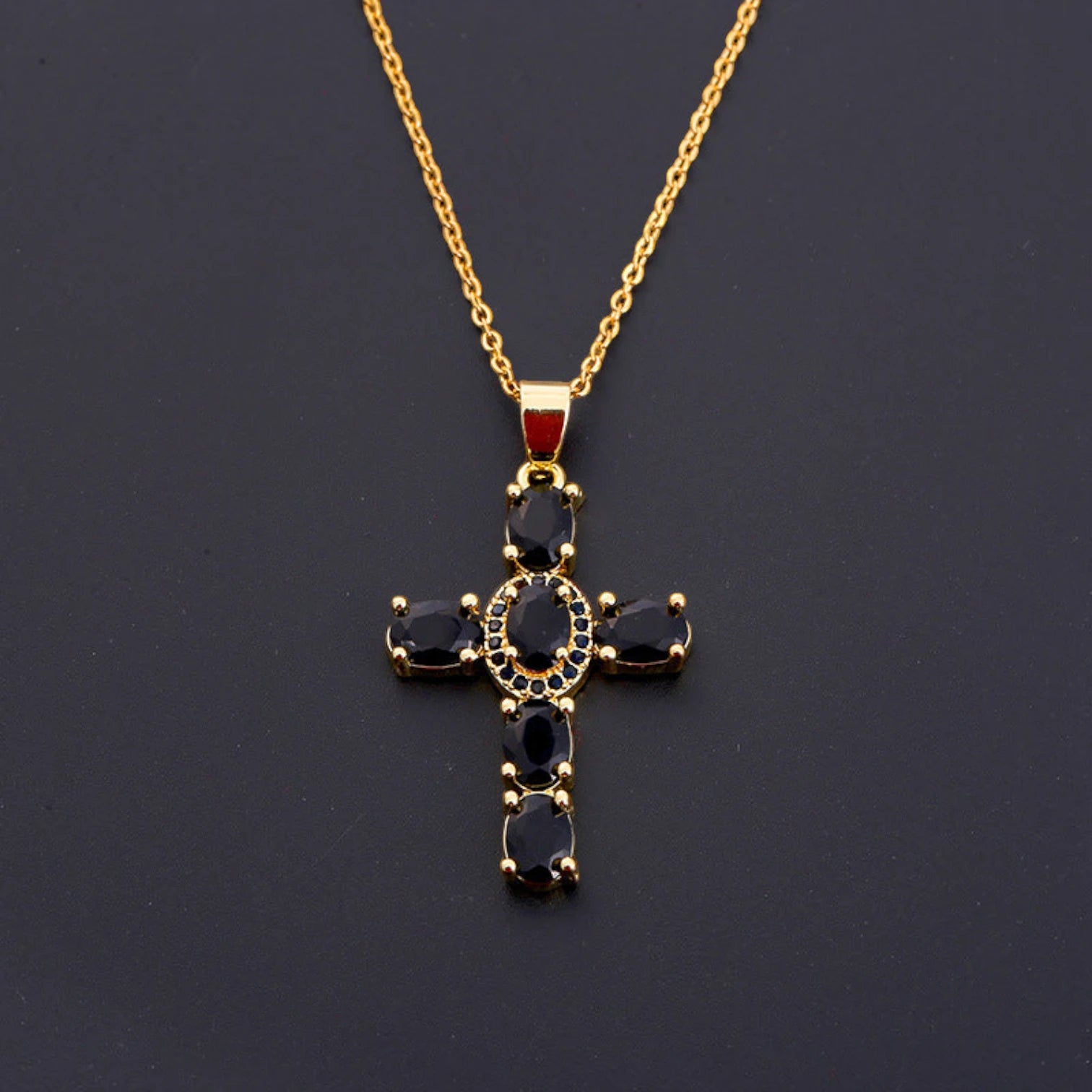 Gold cross necklace with black gemstones on a dark background
